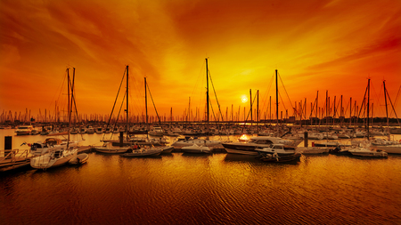 Sailing boats at harbour against red and orange sunset