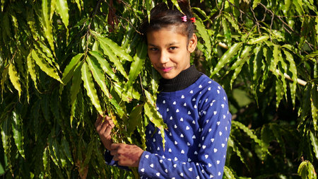 10 January 2021- Chomun, Jaipur, India. Portrait of a smiling girl dressed in blue color in posing with greenish asoca plant leaves background. Selfie concept.のeditorial素材