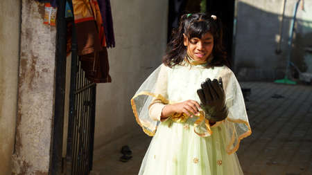 Cute Indian girl in white dress inspecting of black hand glove.の写真素材