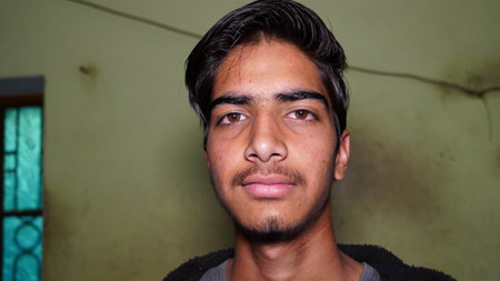 Portrait of a young Indian boy looking with peace at the camera. Isolated facial shot closeup with wall background.のeditorial素材