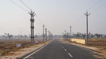 10 February 2021- Sikar, Jaipur, India. Black long asphalt road through electricity poles. Long paving road closeup ends in horizon.のeditorial素材
