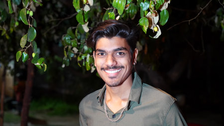 19 February 2021- Sikar, Jaipur, India. Cheerful smiling face of adolescent boy with shiny silver chain. Happy confident Asian boy against camera in a forest tree shadow.のeditorial素材