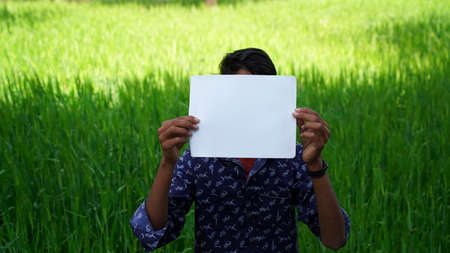 Advertisement and model industry concept. Young Indian boy posing in green field with hiding face...