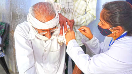 08 April 2021- Akhepura, Sikar, India. Man with face mask getting vaccinated, coronavirus, covid 19 and vaccination concept. Doctor giving antivirus injection to patient.のeditorial素材