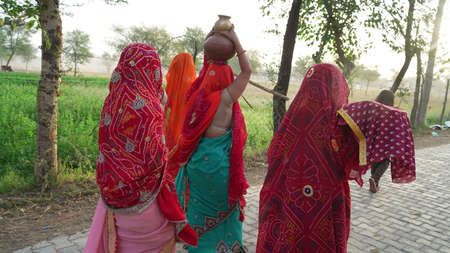 Backside shot of Hindu women with traditional cultured saree. One woman holding a sacred clay pot on...