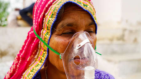 20 May 2021- Reengus, Sikar, India. Old Indian woman infected with Covid 19 disease. Patient inhaling oxygen wearing mask with liquid Oxygen flow.の写真素材
