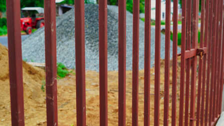 Red metal garden entrance gates set in brick fence with tree covered in building material.の写真素材