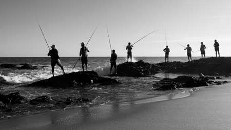 Salvador, Bahia, Brazil - April 25, 2021: Fishermen on rocks with their fishing poles trying to catch fish to sell and consume.のeditorial素材