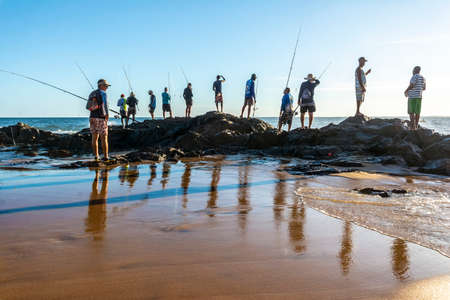 Salvador, Bahia, Brazil - April 25, 2021: Fishermen on rocks with their fishing poles trying to catch fish to sell and consume.のeditorial素材