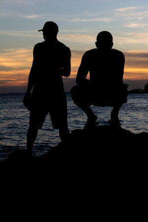 Silhouette of fishermen on the rocks of the Rio Vermelho beach in Salvador, Bahia, fishing for their food and support for their family.の写真素材