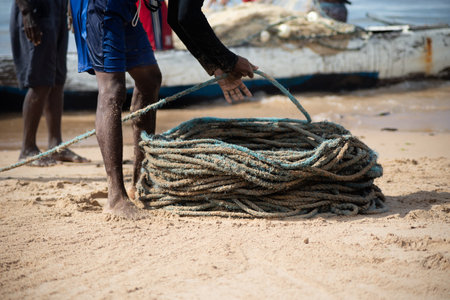 Salvador, Bahia, Brazil - May 23, 2021: Fisherman rolling fishing net to store in warehouse after fishing on Boca do Rio beach.のeditorial素材