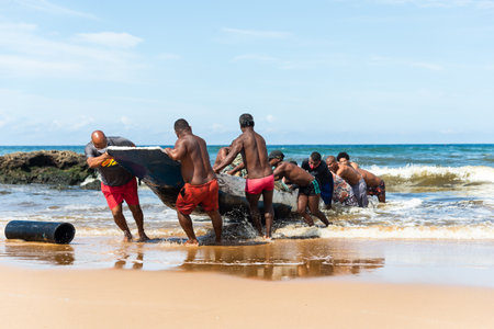Salvador, Bahia, Brazil - May 23, 2021: Fishermen removing their canoe from the sea to place in the Boca do Rio fishermen colony.のeditorial素材