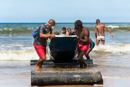 Salvador, Bahia, Brazil - May 23, 2021: Fishermen removing their canoe from the sea to place in the Boca do Rio fishermen colony.のeditorial素材