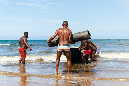 Salvador, Bahia, Brazil - May 23, 2021: Fishermen removing their canoe from the sea to place in the Boca do Rio fishermen colony.のeditorial素材
