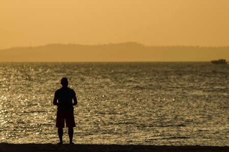 Silhouette of a person at the yellow sunset. Beach of Ribeira, Salvador, Bahia, Brazil.の写真素材
