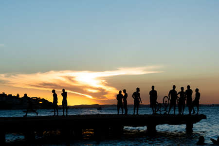 Silhouette of young people jumping from the Crush bridge at the yellow sunset on Ribeira beach in Salvador (BA).の写真素材