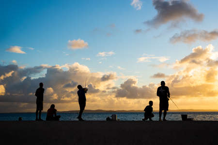 Salvador, Bahia, Brazil - June 06, 2021: Silhouette of fishermen and their poles at Ponta do Humaita, Salvador.のeditorial素材