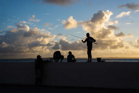 Salvador, Bahia, Brazil - June 06, 2021: Silhouette of fishermen and their poles at Ponta do Humaita, Salvador.のeditorial素材