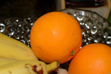 Oranges and bananas in a glass vase on the table. Fresh fruit for breakfast.の写真素材