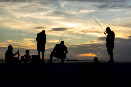 Salvador, Bahia, Brazil - April 11, 2021: Silhouette of fishermen with their poles at sunset.の写真素材