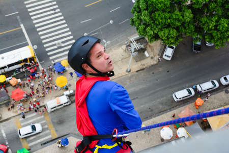 Man dressed as a superhero rappelling down from a tall building. Salvador Bahia Brazil.