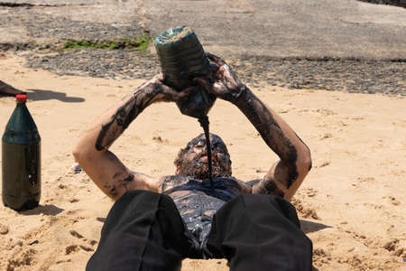 Man putting oil on himself in protest of oil spilled on the beaches of Brazil in 2019. Performance...
