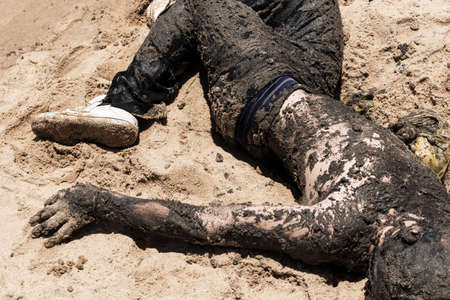 Man covered in oil on the beach at Porto da Barra in Salvador, Bahia, in protest of oil spilled by a ship on the beaches of Brazil.の写真素材