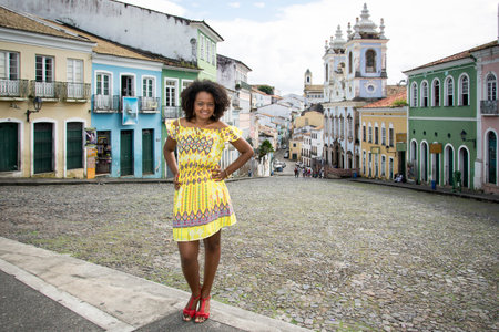 Model in a yellow dress smiling, looking and posing at the camera. In the background, the historical...
