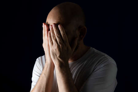 Person with hands on face against dark background. Salvador, Bahia, Brazil.の写真素材