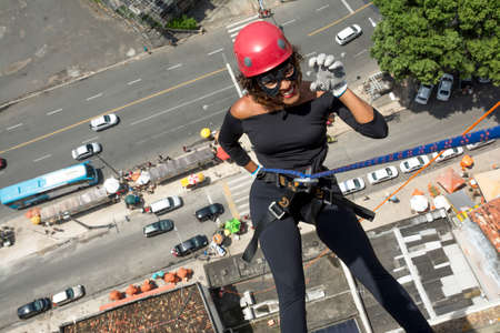 A woman wearing a hero costume with protective helmet walking down a tall Rappel building. Salvador Bahia Brazil.の写真素材
