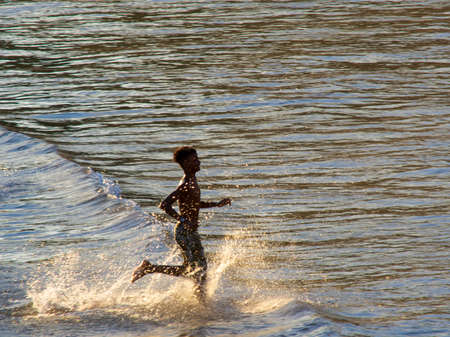 Salvador, Bahia, Brazil - January 05, 2019: Young man running in the waters and sand of Paciencia beach in Rio Vermelho. Salvador Bahia Brazil.のeditorial素材