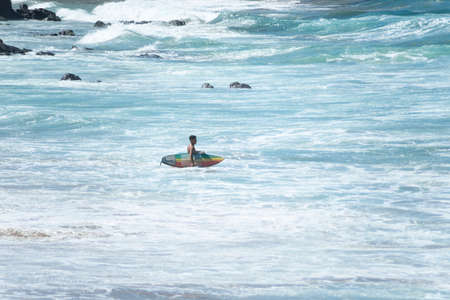 Salvador, Bahia, Brazil - August 15, 2021: Surfer entering the sea to surf at Farol da Barra beach...