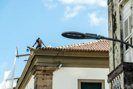 Salvador, Bahia, Brazil - June 17, 2021: Construction worker on top of roof repairing structure.