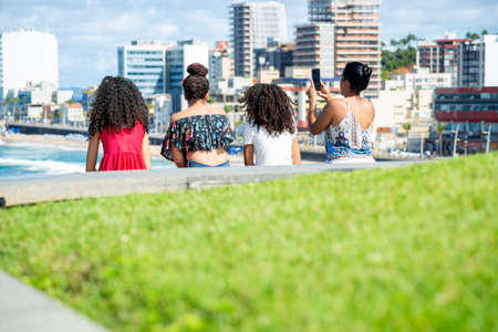 Salvador, Bahia, Brazil - August 15, 2021: Back of four women against sea and city landscape. Salvador Bahia Brazil.のeditorial素材