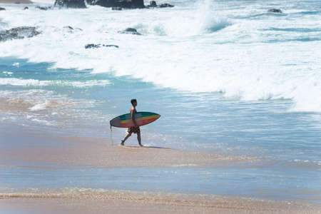 Salvador, Bahia, Brazil - August 15, 2021: Surfer entering the sea to surf at Farol da Barra beach in the Brazilian city of Salvador.のeditorial素材