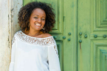Model in a white dress smiling, looking and posing at the camera. In the background, the historical...