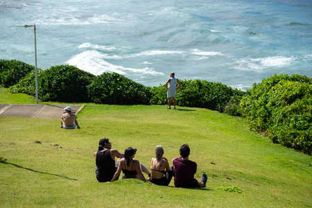 Salvador, Bahia, Brazil - August 15, 2021: People sitting on the grass enjoying the landscape of Farol da Barra beach in Salvador, Bahia, Brazil.のeditorial素材