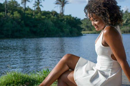 Beautiful model in a white dress smiling and looking at the camera. In the background, trees, plants, flowers and the river in the landscape. Salvador Bahia Brazil.の写真素材