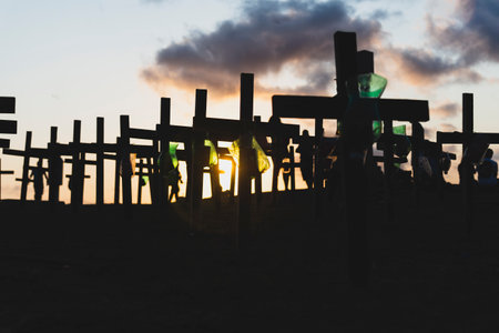 Silhouette of people and crosses fixed on the ground in honor of those killed by covid-19. Sunset in...