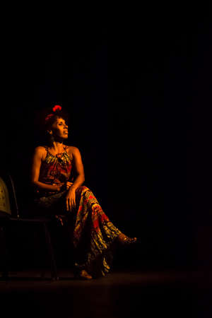 Actress sitting on a chair in the theater playing a character in a show. Black background. Salvador Bahia Brazil.の写真素材
