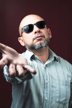Portrait of a bearded and bald man wearing eyeglasses against a red dark background. Salvador,...