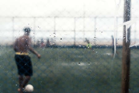 Wet glass, inside car view of people playing ball. Salvador, Bahia, Brazil.