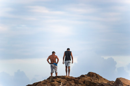 Salvador, Bahia, Brazil - September 26, 2021: Two men and standing on a big rock at Farol da Barra beach in Salvador city, Bahia state, Brazil.のeditorial素材
