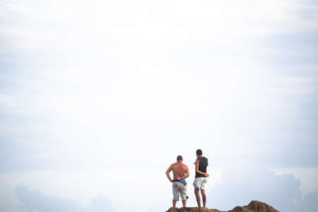 Salvador, Bahia, Brazil - September 26, 2021: Two men and standing on a big rock at Farol da Barra beach in Salvador city, Bahia state, Brazil.のeditorial素材