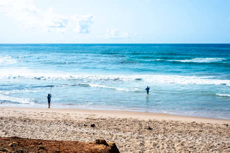 Salvador, Bahia, Brazil - October 10, 2021: Two fishermen with fishing rod on the beach of Boca do...