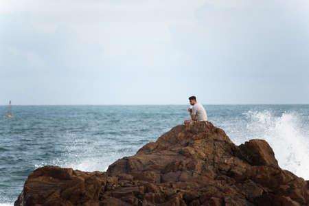 Salvador, Bahia, Brazil - September 26, 2021: Man sitting on a big rock at Farol da Barra beach in Salvador city, Bahia state, Brazil.のeditorial素材