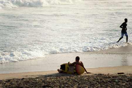 Salvador, Bahia, Brazil - September 26, 2021: Surfer sitting on the beach sand looking at the sea. Farol da Barra beach in Salvador, state of Bahia, Brazil.のeditorial素材