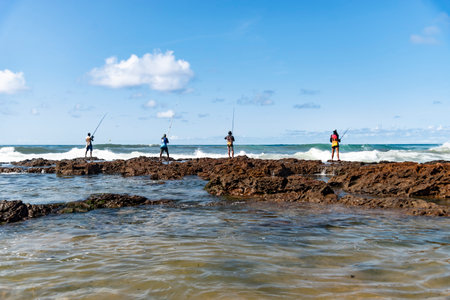 Salvador, Bahia, Brazil - October 10, 2021: Fishing men on top of the rocks of Rio Vermelho beach fishing with pole, City of Salvador, capital of Bahia, Brazilのeditorial素材