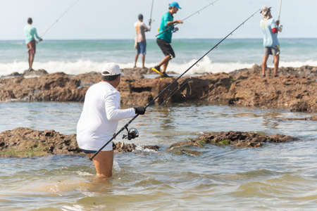 Salvador, Bahia, Brazil - October 10, 2021: Fishermen with fishing rod on the rocks fishing on the famous Boca do Rio beach in Salvador, capital of Bahia, Brazilのeditorial素材