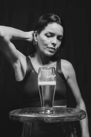 Black and white portrait of a woman and a glass with liquid against black background. Salvador, Bahia, Brazil.の写真素材